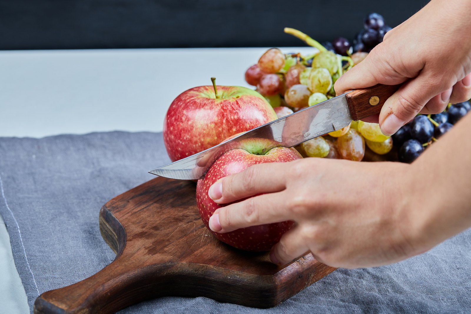 Mains coupant une pomme sur une planche avec une grappe de raisin