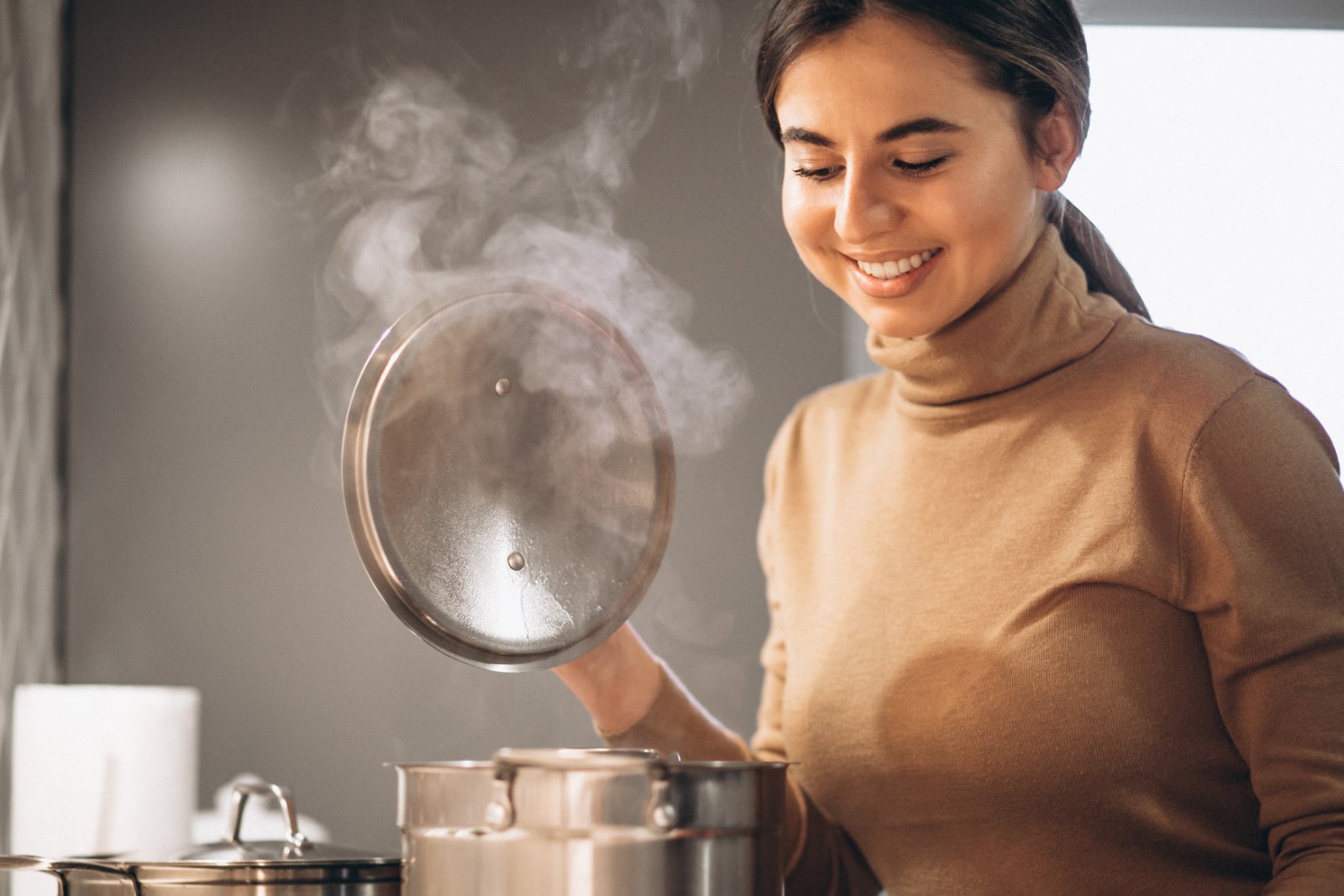 Cuisinière souriante soulevant le couvercle d'une marmite fumante