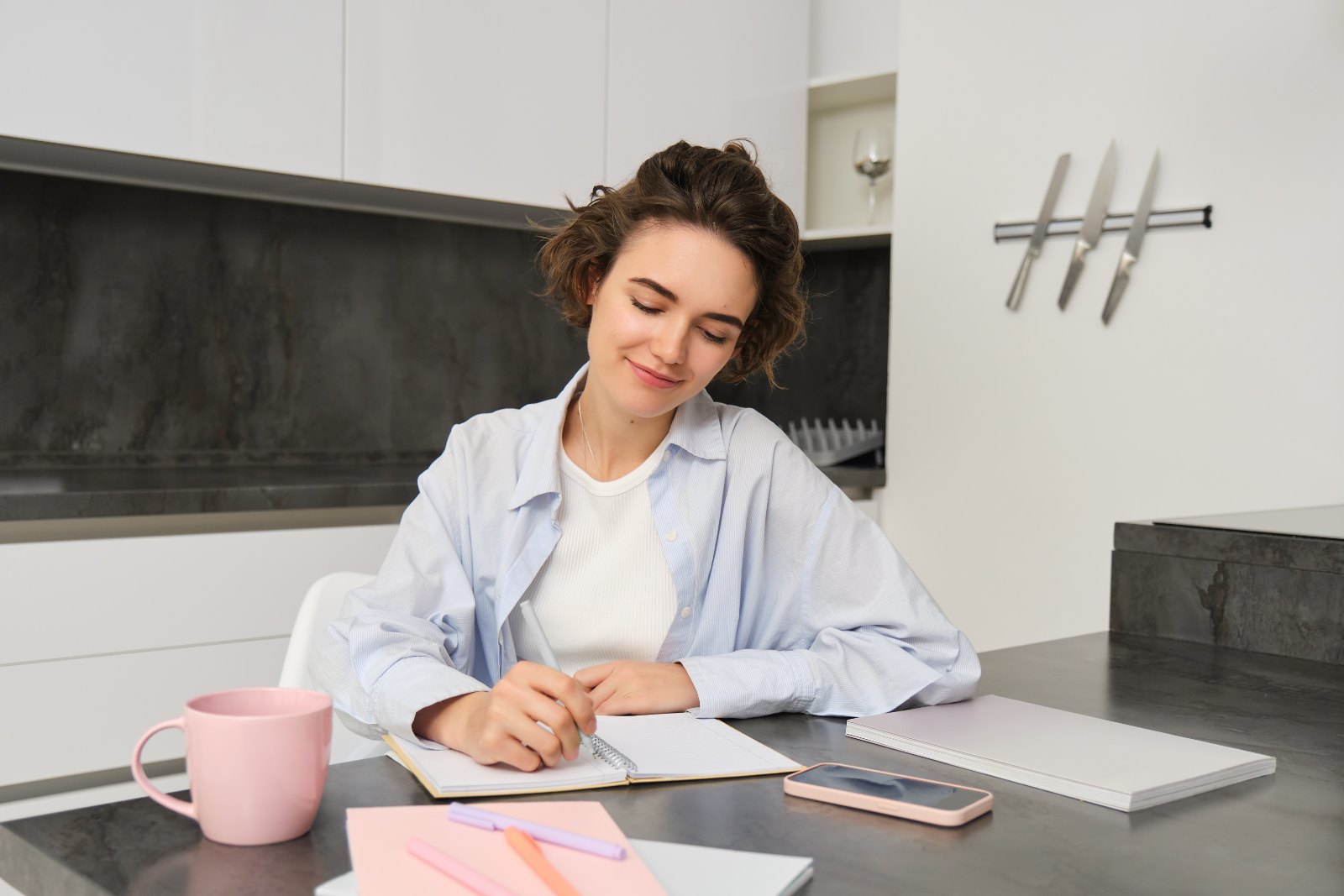 Femme assise dans sa cuisine, écrivant son planning de repas dans un carnet