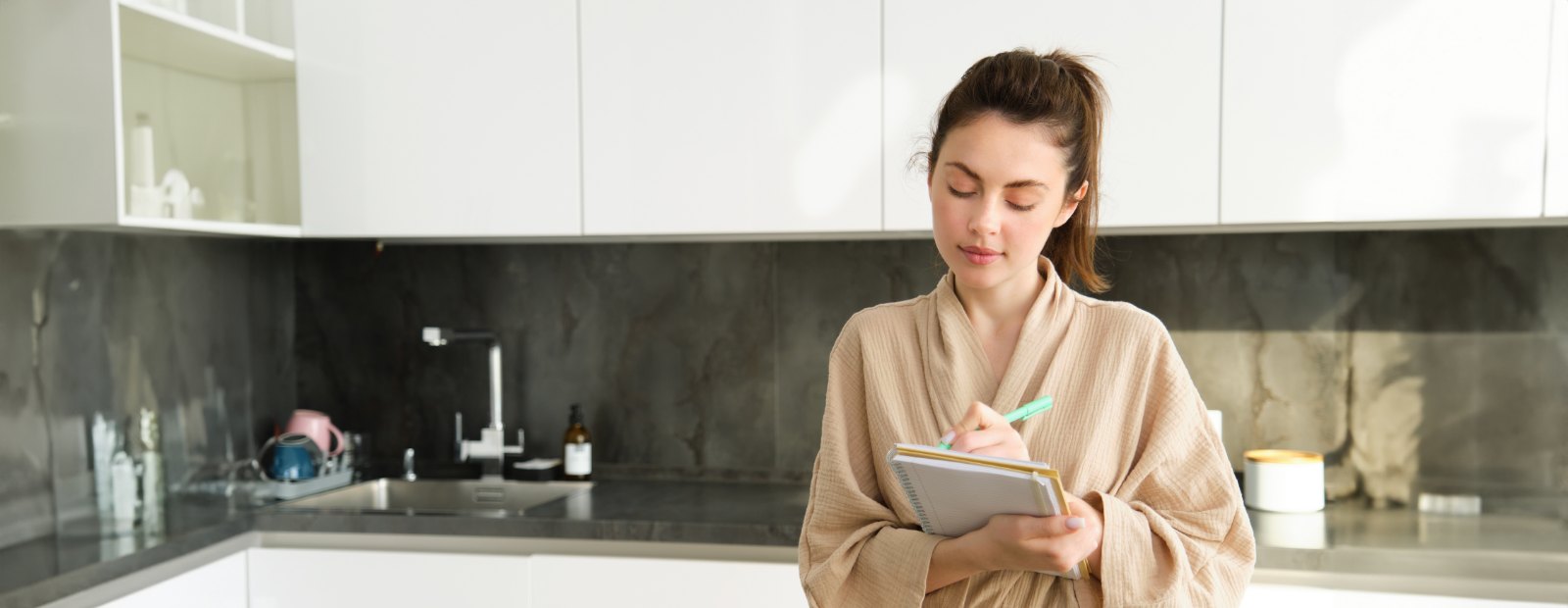 Femme notant son plan de repas dans sa cuisine : moins de charge mentale en semaine