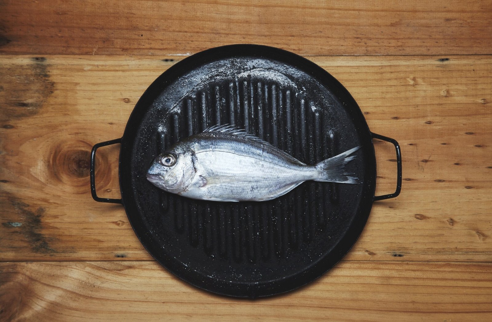 Dorade de mer entière posée sur une poêle-gril, prête pour un dîner simple