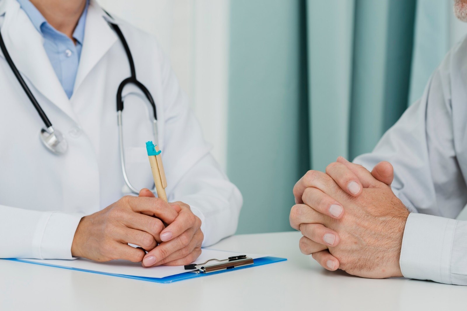 Médecin et patient en consultation, mains posées sur le bureau près d’un dossier
